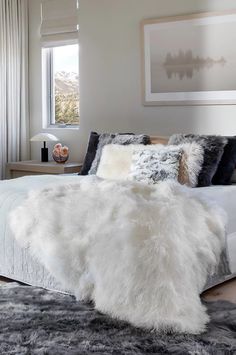 a bed with white fur on top of it in a bedroom next to a window