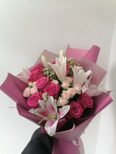 a bouquet of pink roses and white lilies in a vase with someone's hand