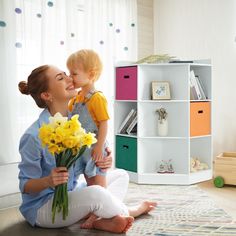 a woman sitting on the floor holding a bouquet of flowers with a child standing next to her