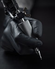 a person in black gloves holding a metal object with a pen on top of it