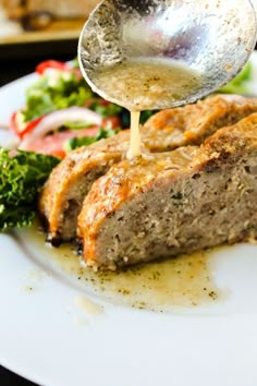 a plate with meat, vegetables and sauce being drizzled on it by a spoon