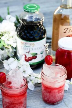 two glasses filled with ice and cherries next to bottles of alcohol on a table