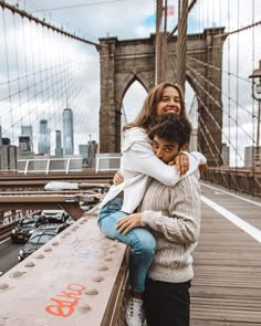 two people hugging each other in front of the brooklyn bridge with words written on it