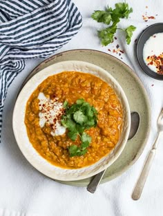 a white bowl filled with red lentula soup and topped with sour cream, cilantro and parsley