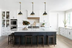 a large kitchen with white cabinets and black counter tops, three stools in front of the island