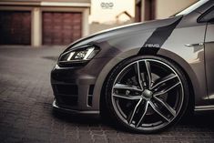 the front end of a grey car parked on a brick road with garage doors in the background