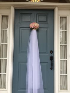 a bride's veil hanging on the front door of a house with flowers in it