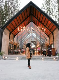 a woman standing in front of a grandis entrance with lights on the side walk