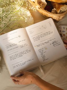 an open book sitting on top of a table next to a basket filled with flowers