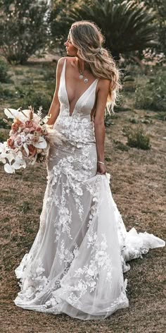 a woman in a wedding dress is walking through the grass with flowers on her bouquet