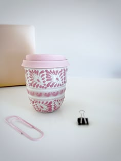 a pink and white coffee cup sitting on top of a table next to a paper clip