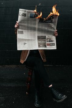 a person sitting on a chair holding up a newspaper with flames coming out of it