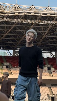 a young man standing in front of an empty stadium bleachers with his hand on his hip