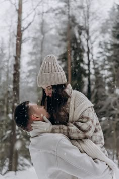 a man and woman kissing in the snow with trees in the background