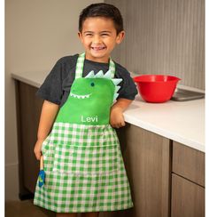 a young boy wearing an apron and smiling at the camera while standing next to a counter