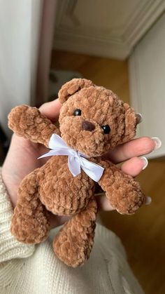 a person holding a small brown teddy bear in their left hand and wearing a white bow