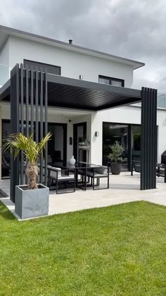 a modern house with an outdoor patio and dining area in the back yard, on a cloudy day