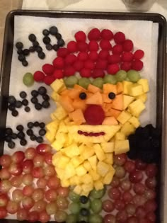 a tray filled with grapes, fruit and a clown face