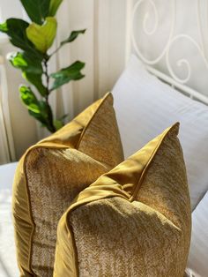 two yellow pillows sitting on top of a white bed next to a green potted plant