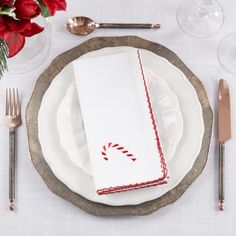 a white plate topped with a candy cane napkin next to silverware and red flowers