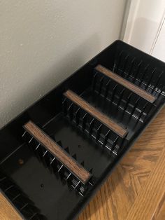 three black trays with wooden dividers sitting on top of a wood floor next to a white wall