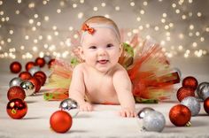 a baby is laying on the floor surrounded by christmas ornaments and balls, smiling at the camera