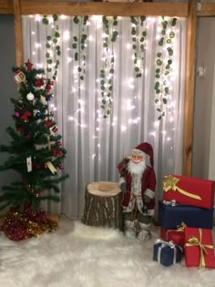 a santa clause standing next to presents in front of a christmas tree with lights on it