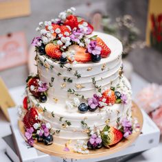 a wedding cake with strawberries, blueberries and flowers on the top is ready to be cut