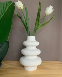 a white vase with flowers in it on a table