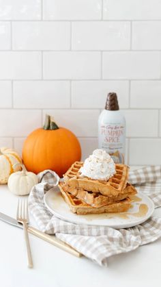 a stack of waffles on a plate with whipped cream and pumpkins in the background