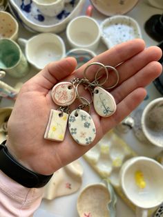 a hand holding several different key chains in front of cups and saucers on a table