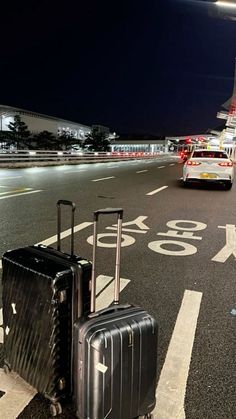 two pieces of luggage are sitting on the side of the road near an airport at night