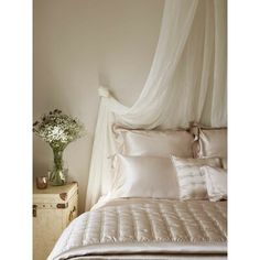 a white bed topped with lots of pillows next to a night stand and vase filled with flowers