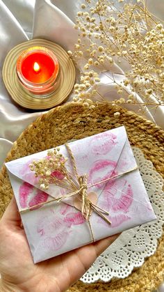 a hand holding a small envelope with pink ink on it and a lit candle in the background