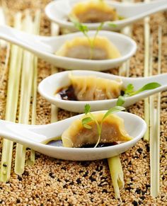 three white spoons with food on them sitting on a counter top next to chopsticks