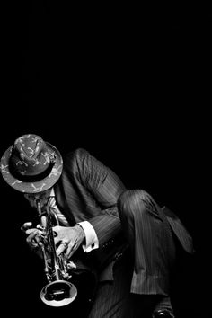 a man in a suit and hat leaning over with his foot on a saxophone while wearing a fedora