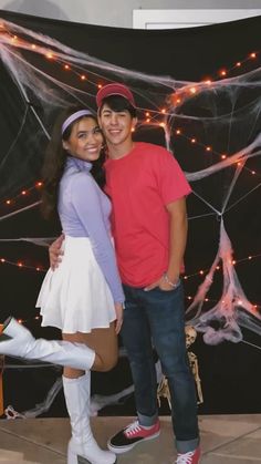 a man and woman pose for a photo in front of a spider web backdrop with lights