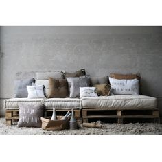 a couch made out of wooden pallets with pillows on the top and bottom, in front of a concrete wall