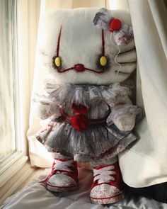 a teddy bear dressed up as a clown with red shoes and white dress sitting in front of a curtain