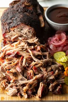 a wooden cutting board topped with meat and veggies next to a bowl of dipping sauce