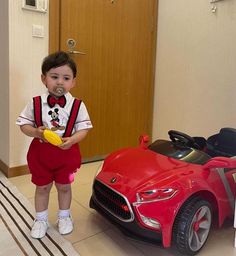 a little boy standing next to a red toy car