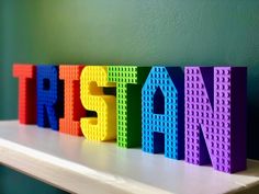 the letters are made out of legos on top of a white shelf in front of a gray wall