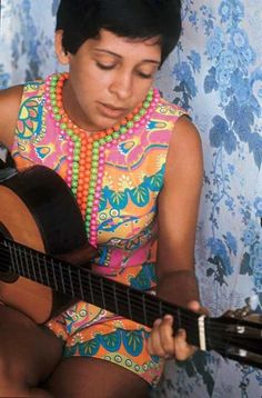 a woman in a colorful dress playing an acoustic guitar