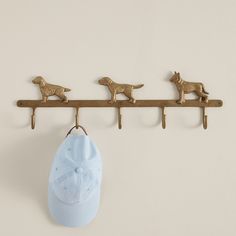 three brass dog hooks hang on a wall next to a baseball cap