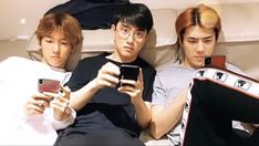 three young men laying on a bed looking at their cell phones and taking pictures with them