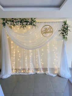 a white wedding backdrop with flowers and greenery on the top is decorated with lights