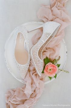 a pair of white shoes sitting on top of a plate next to a pink flower