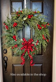 a christmas wreath on the front door with red berries and greenery hanging from it