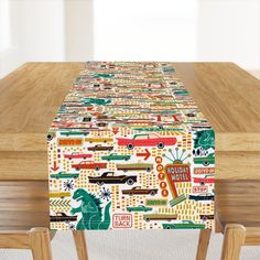 the table is covered with colorful cars and trucks on it, along with wooden chairs