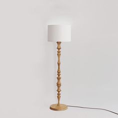 a wooden floor lamp with a white shade on the base and a cord attached to it